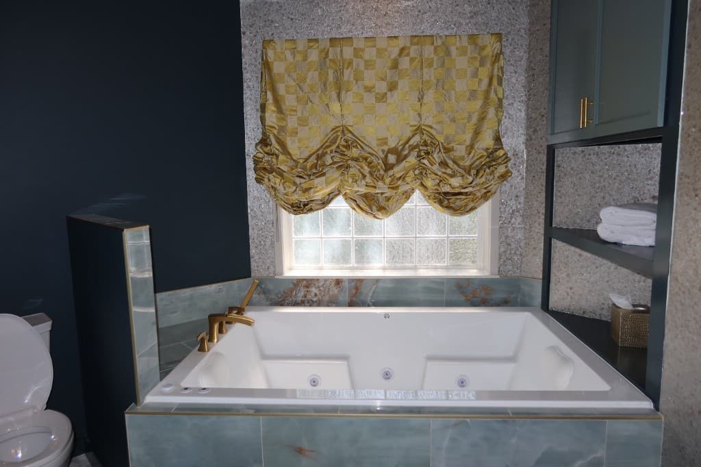 Luxury bathroom with jetted tub, teal marble tile surround, gold trim, and built-in storage