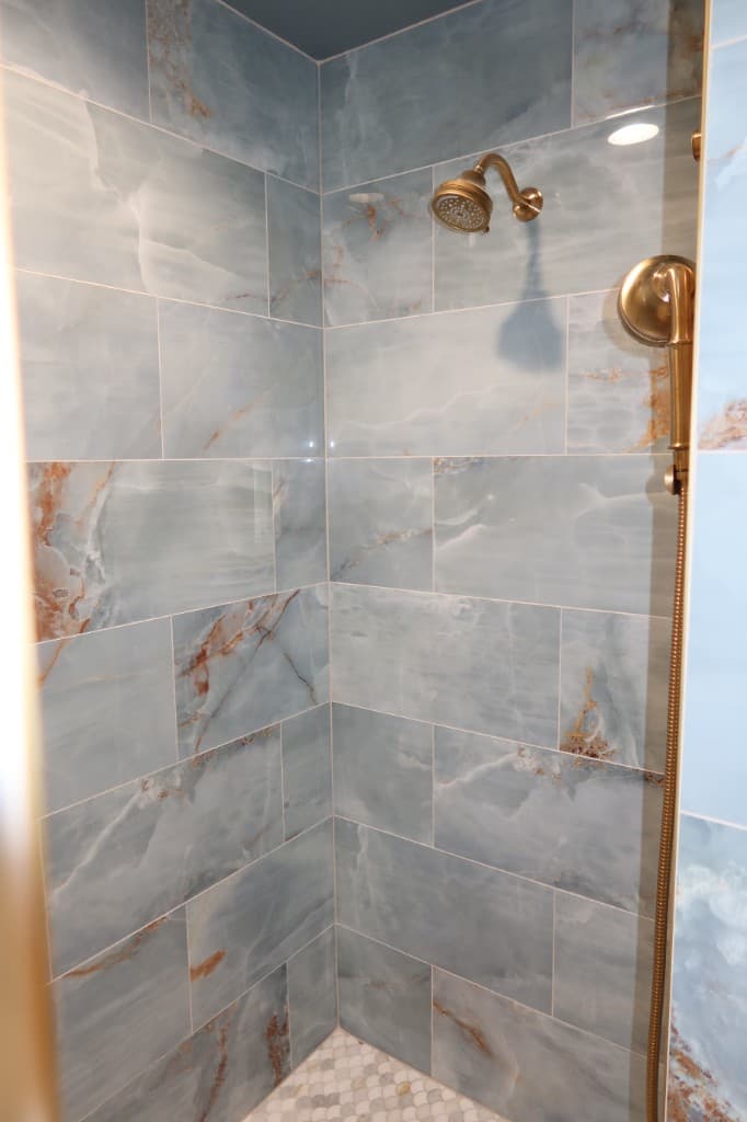 Walk-in shower with blue marble wall tiles, brushed gold fixtures, and scalloped mosaic floor