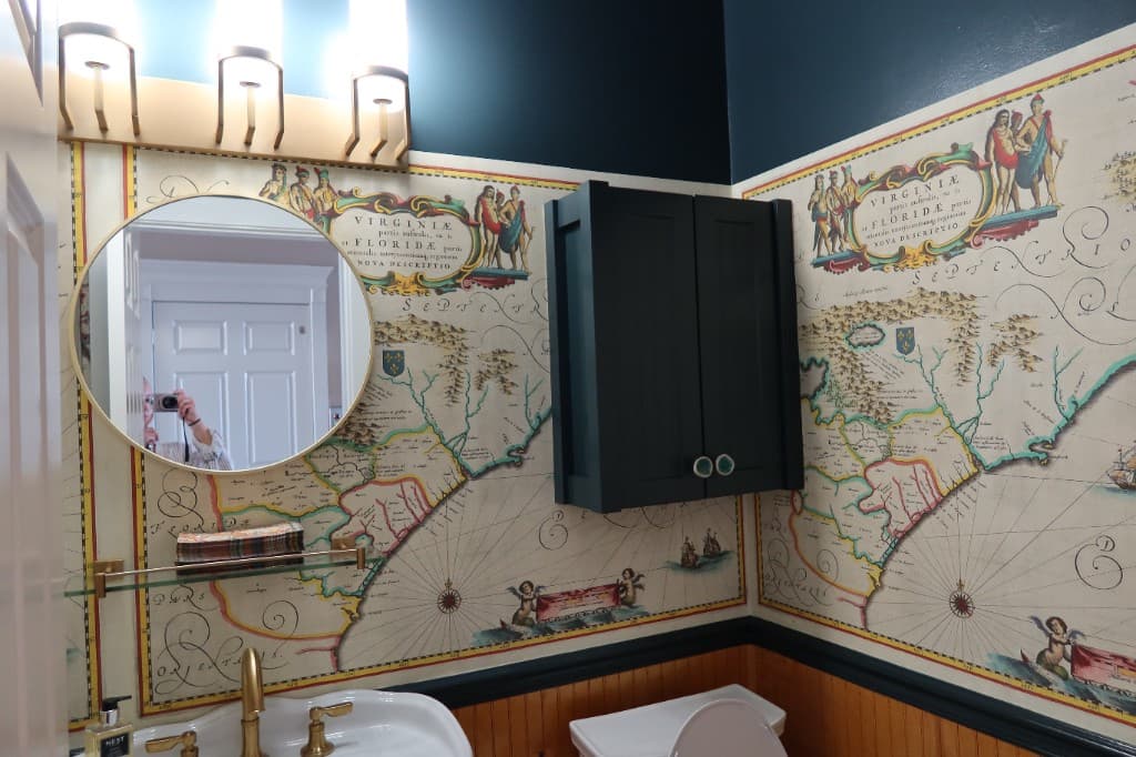 Bathroom with vintage map wallpaper, wainscoting, and brass fixtures
